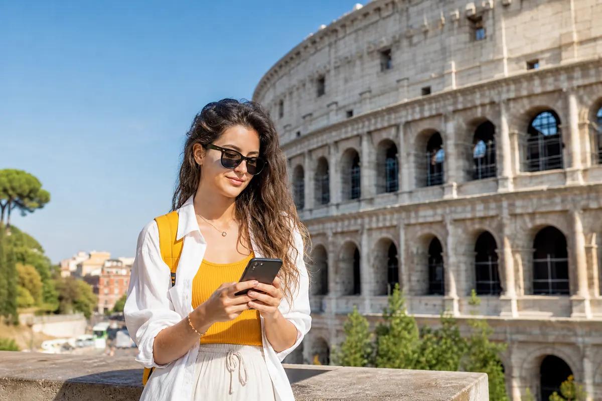 Female traveler in sunglasses checking her smartphone in front of a Roman amphitheatre
