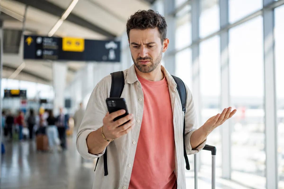 Voyageur agacé haussant les épaules devant son smartphone dans une passerelle d'aéroport lumineuse