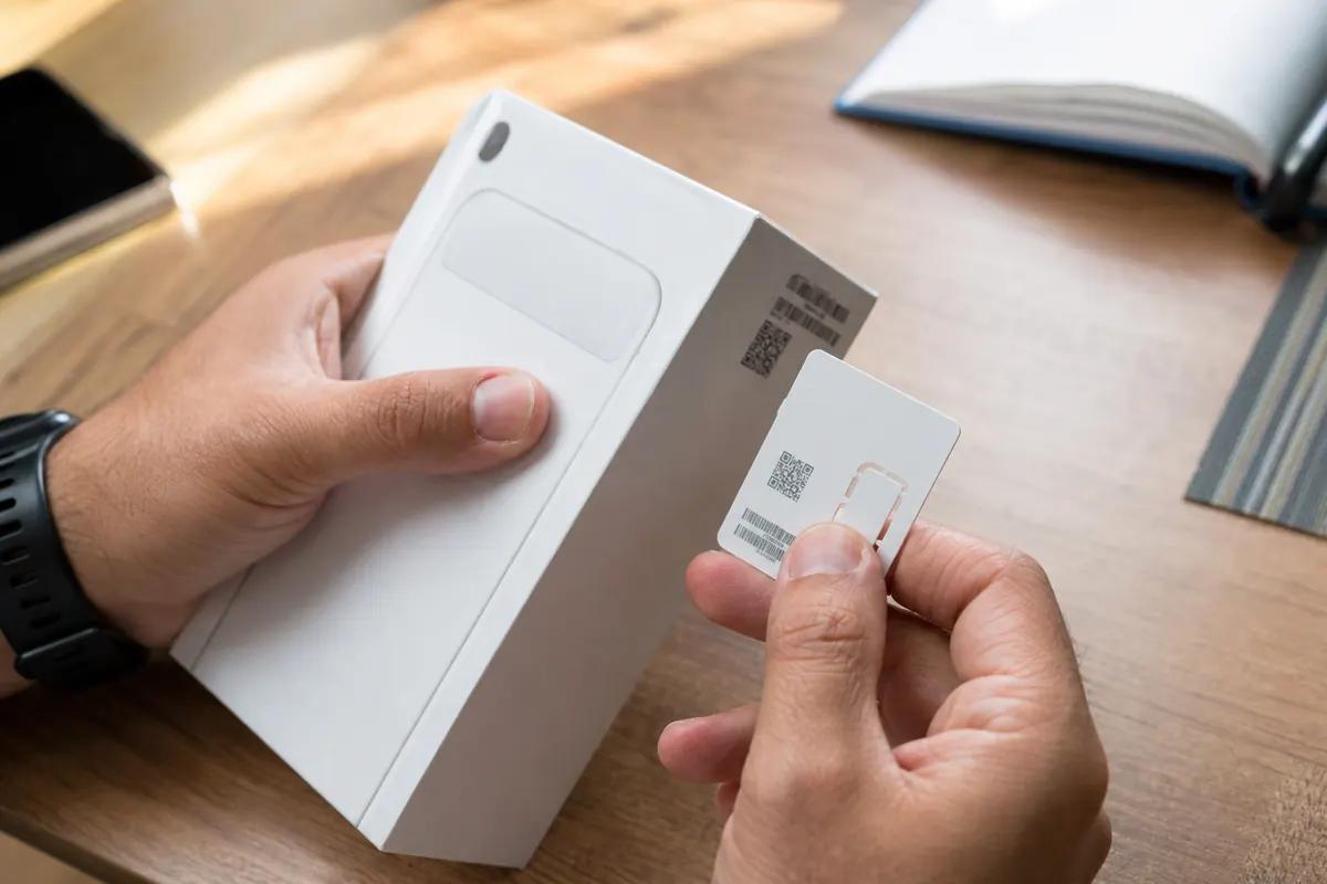 Mains tenant la boîte d'un smartphone et une carte SIM à QR code au-dessus d'un bureau en bois