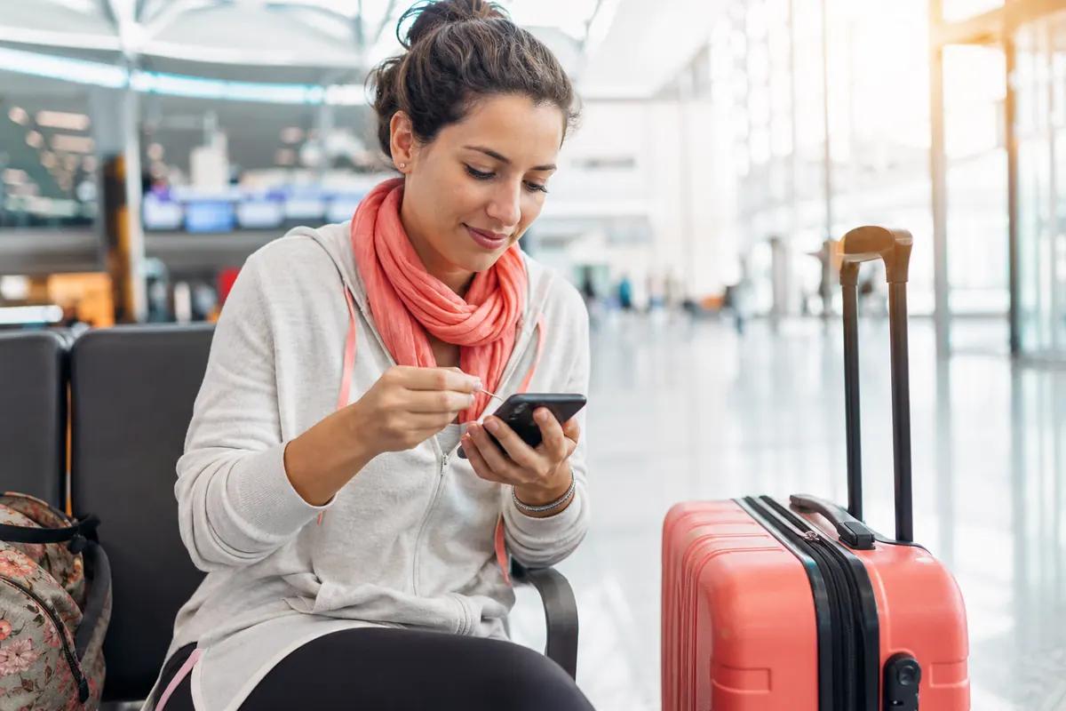 Voyageuse assise en salle d'embarquement insérant une fine tige dans le tiroir SIM de son téléphone