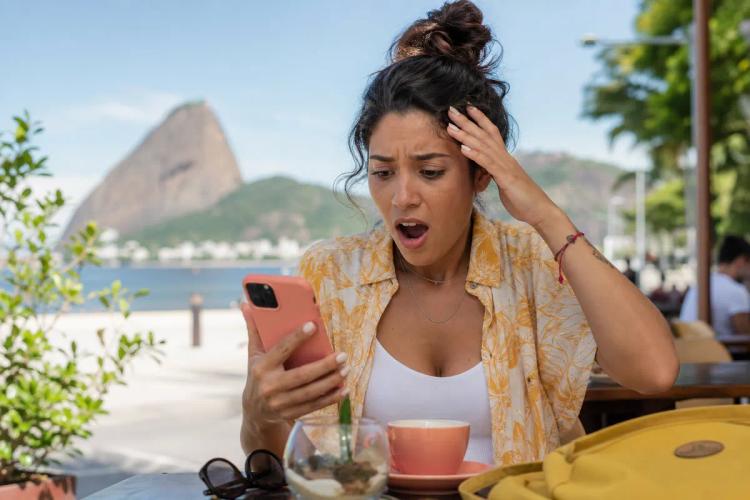 Voyageuse stupéfaite devant son smartphone en terrasse, le Pain de Sucre de Rio en arrière-plan