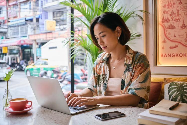 Woman working on her laptop in a Bangkok cafe, smartphone resting on the table beside her